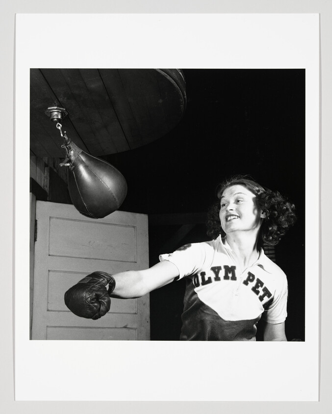 Young woman smiling as she punches a hanging speed bag in a training room.