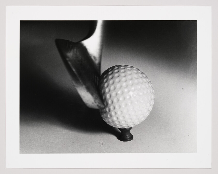 A golf club about to strike a dimpled golf ball balanced on a small tee.