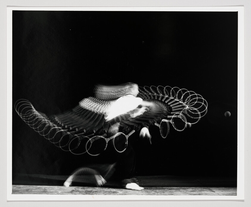 Tennis player captured in multiple exposures swinging a racket toward a ball.