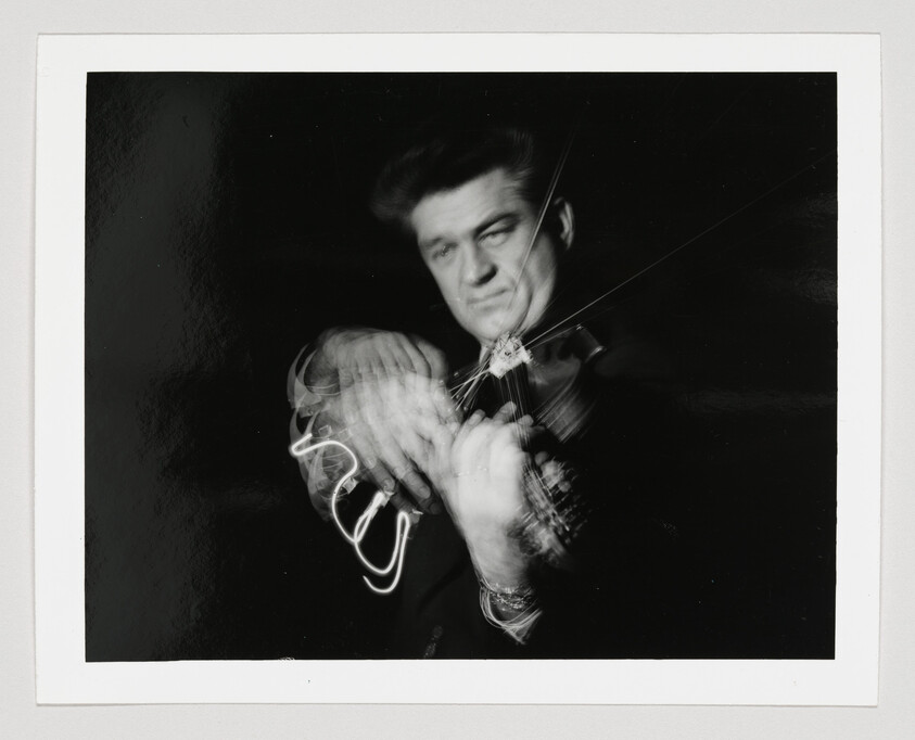 A man intensely playing a violin, his hands and bow blurred by fast motion.