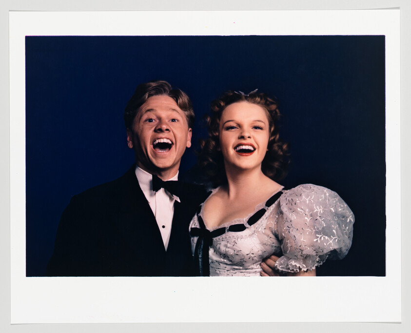 A young man in a tuxedo and a young woman in a white puff-sleeved dress smiling broadly together.