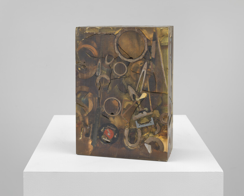 Bronze rectangular block sculpture embedded with rusted tools and circular metal pieces on a white pedestal.