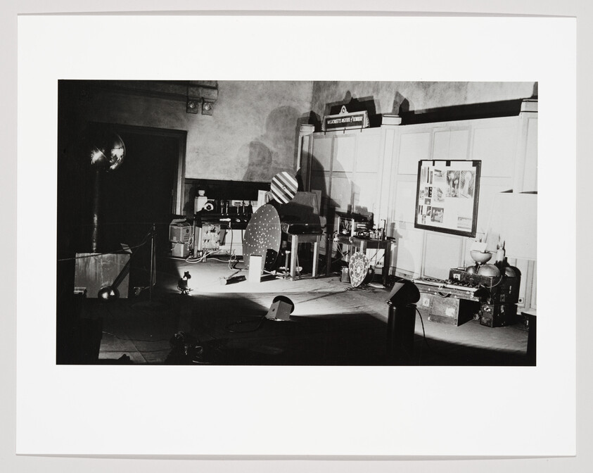 Stage with vintage film and audio equipment under spotlights, scattered cables and control panels.