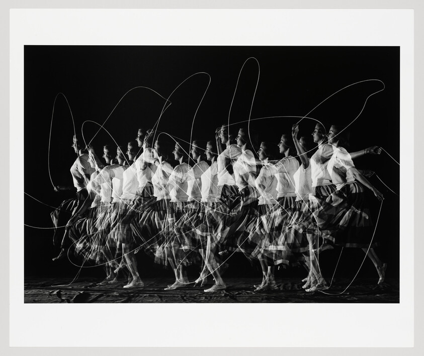 Woman repeatedly jumping rope across the frame, captured in layered long-exposure motion.