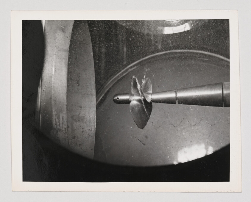A metal drill bit with two curved blades mounted on a rotating shaft inside a machine.