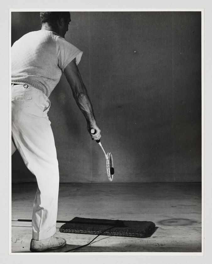 A man practices swings with a racket, hitting a ball tethered to a mat on the floor.