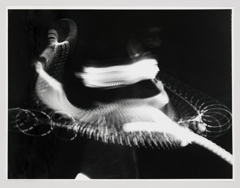 Blurred figure moving rapidly with looping light trails creating repeated circular and spine-like patterns.