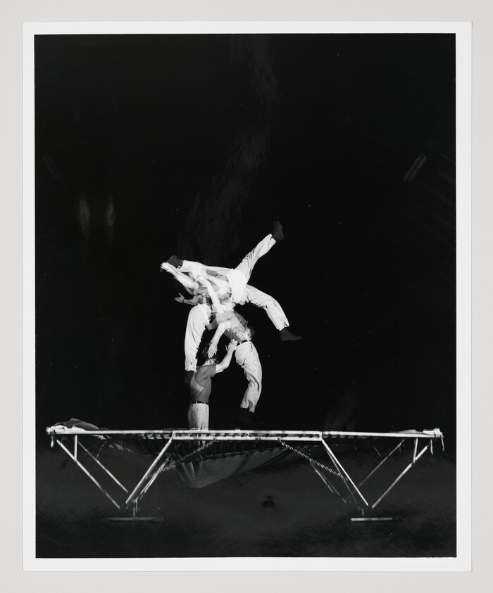 Two acrobats perform a midair flip above a trampoline during a synchronized stunt.