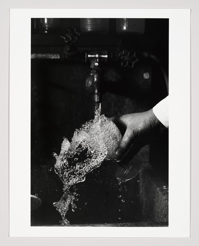 A hand holds a glass under a running tap as water splashes and bubbles over it.