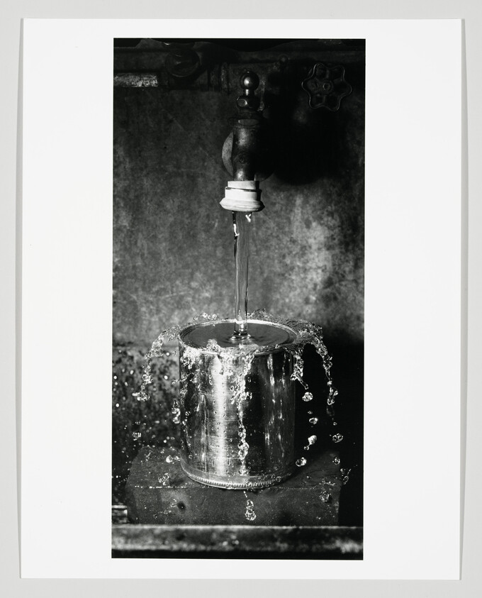 A metal can under a faucet overflows as water pours in and splashes outward.