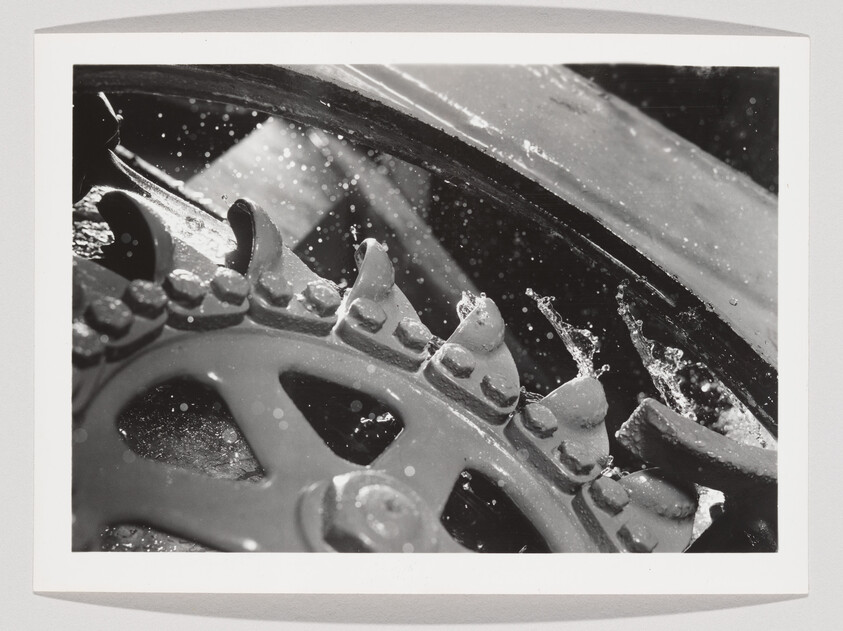 Rusty metal gear teeth rotating while water splashes and droplets fly from the mechanism.