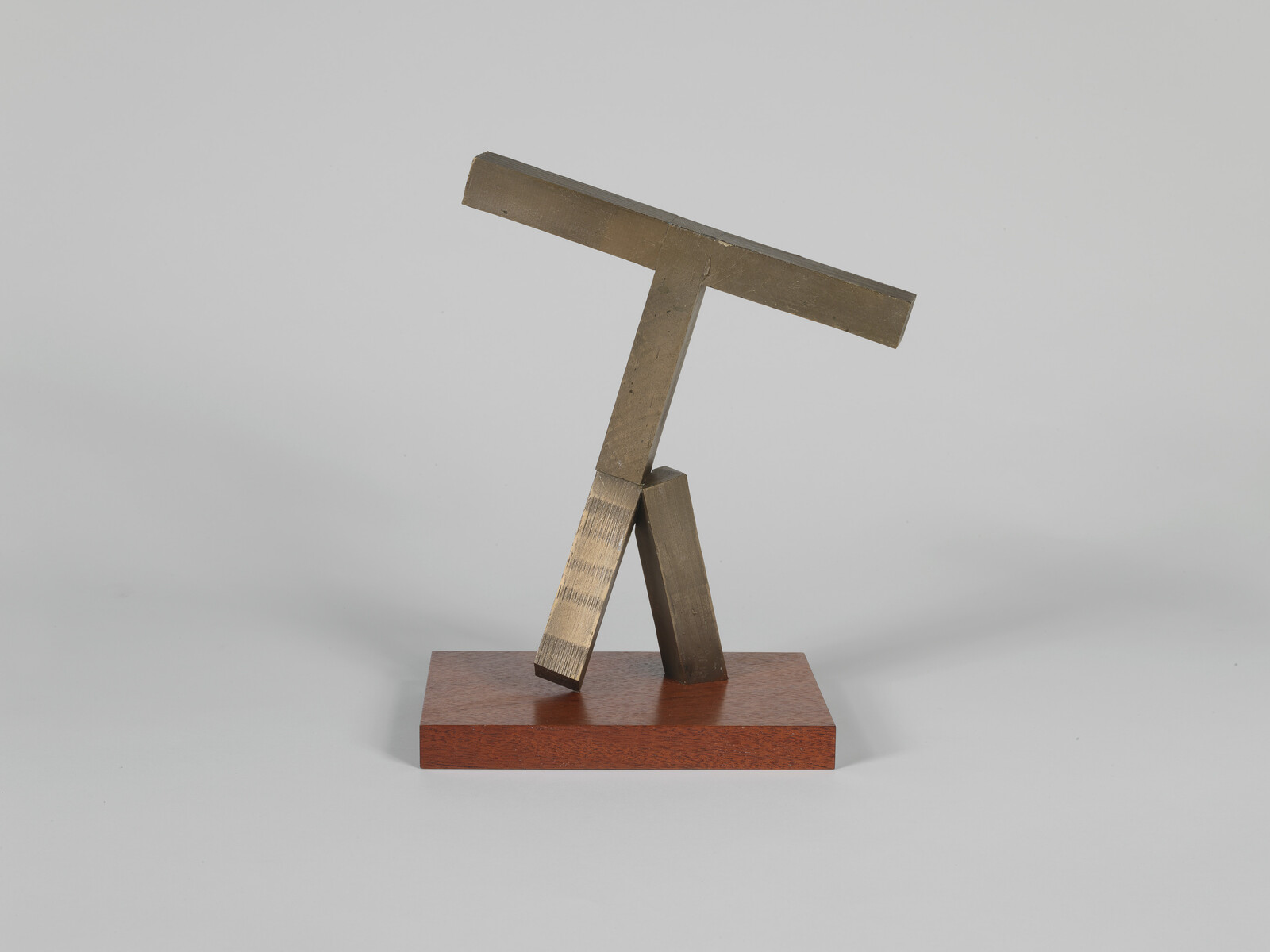 Small bronze abstract sculpture of angled T-shaped bars balanced on a low wooden base.