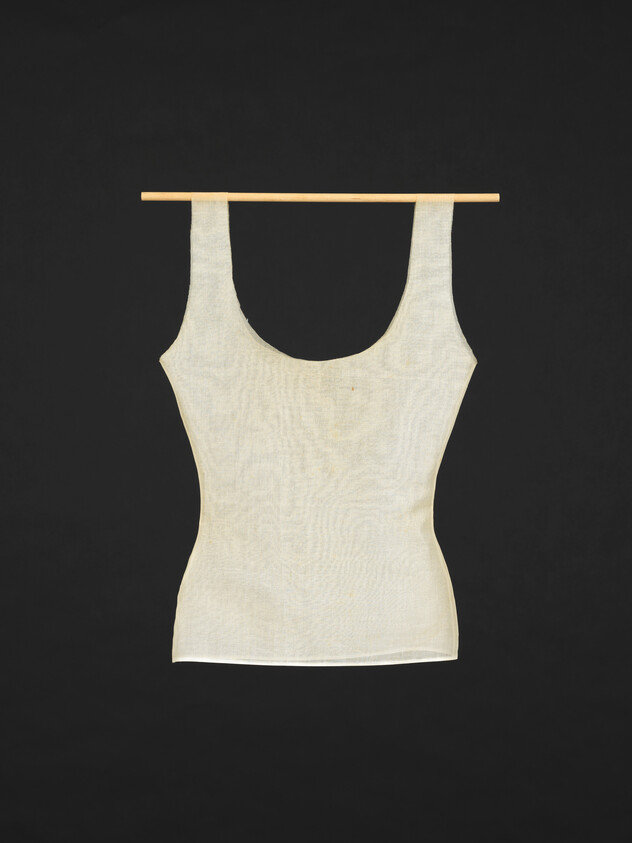 Beige sleeveless tank top hanging from a thin wooden rod against a black background.