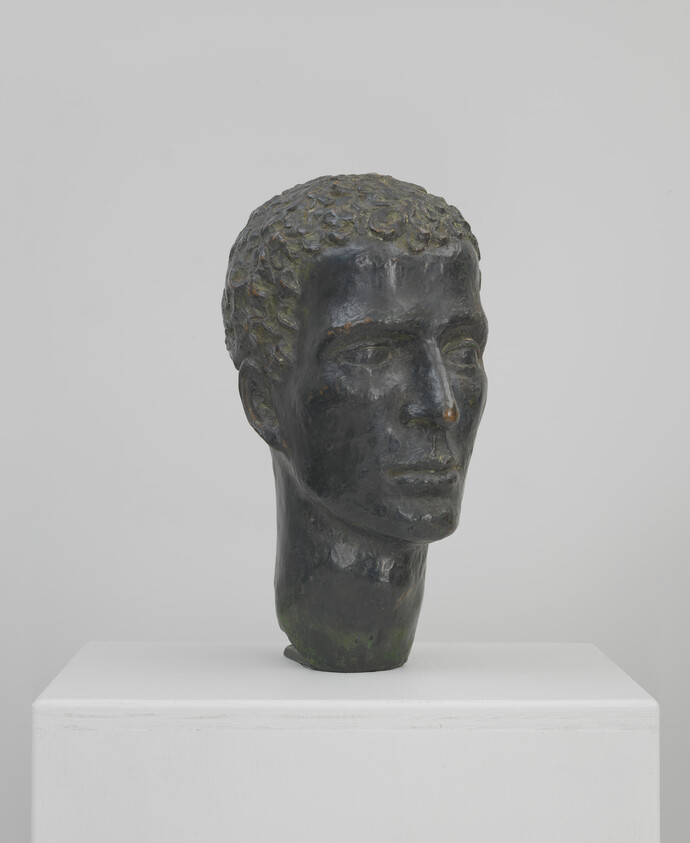 Bronze sculpted male head with short curly hair displayed on a white pedestal.