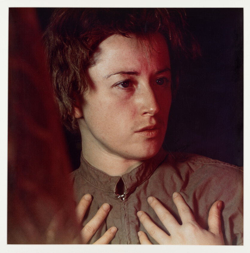 Young person with short hair looks to the side with hands pressed to their chest.