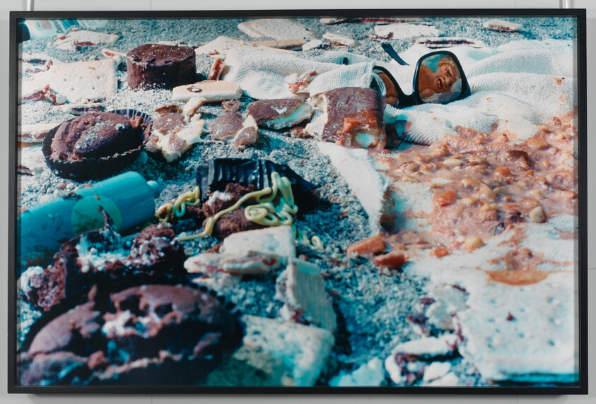Scattered broken cookies, crackers, condiments, and sunglasses on a sandy towel.