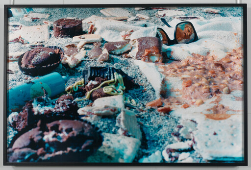 Scattered broken cookies, crackers, condiments, and sunglasses on a sandy towel.