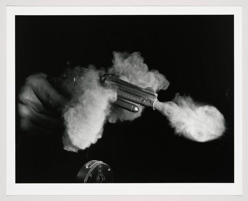 Hand-held revolver firing with bright muzzle flash and thick smoke spreading from the barrel.