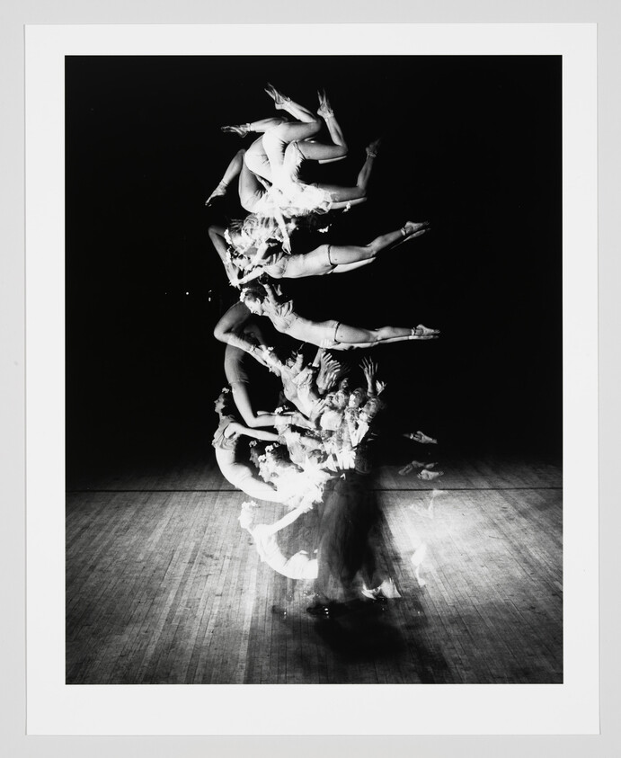 A dancer captured in multiple overlapping leaps across the stage through long-exposure motion.