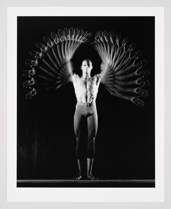 Male dancer stands center while his blurred arms move upward creating a fan-like wing pattern.