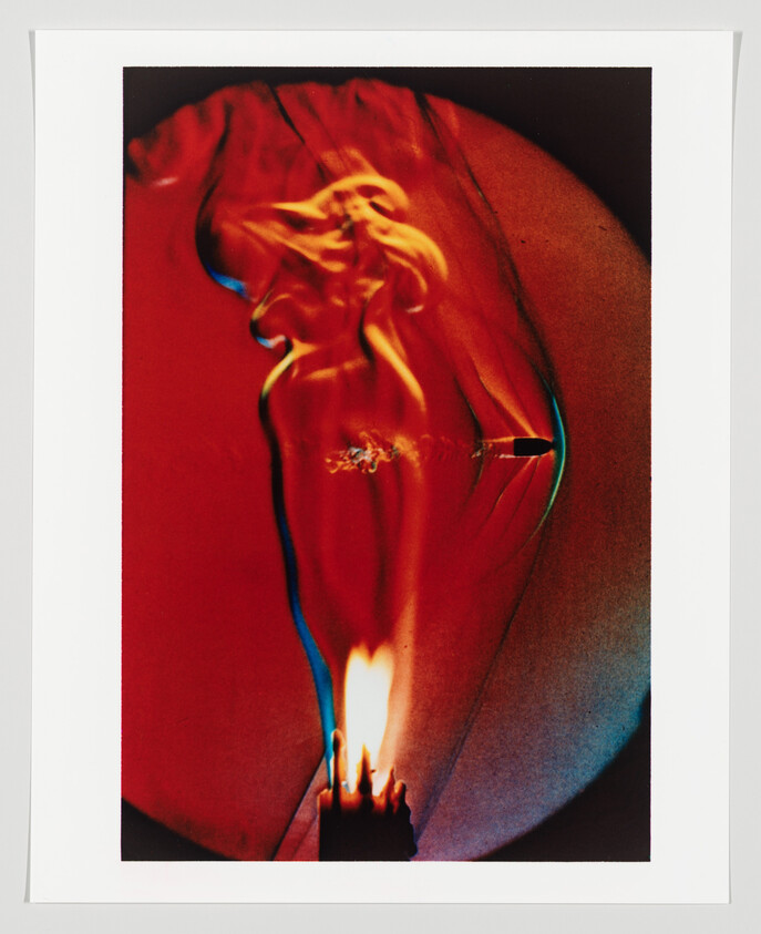 A striking artistic photograph depicting a lit match with a vibrant flame, casting a colorful, abstract silhouette resembling a dancing figure against a red and orange backdrop.