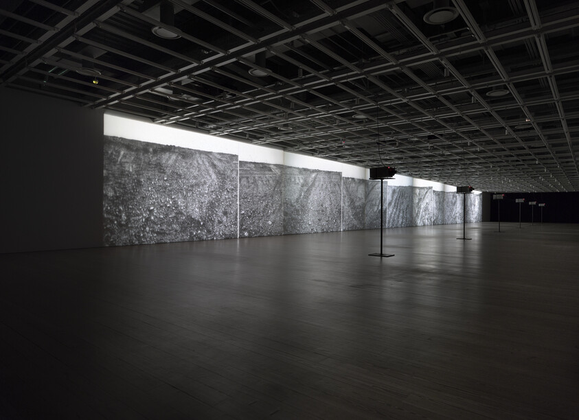 Large, dark room with several projectors displaying black and white textured images across a long wall.