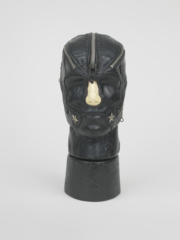 Black leather head sculpture with zippers and a prominent white nose, featuring star-shaped decorations.