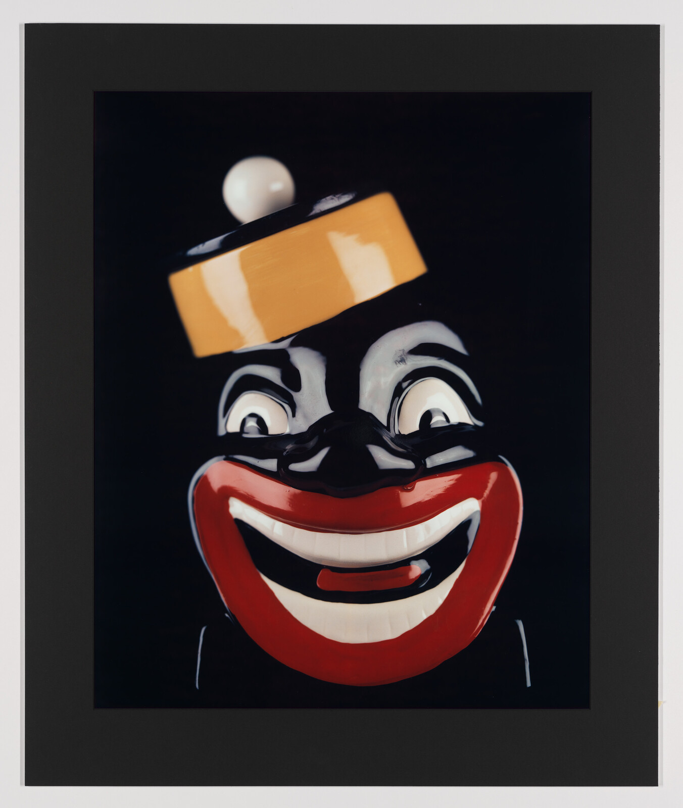 A glossy black caricature face with oversized red lips, wide eyes, and a yellow hat.