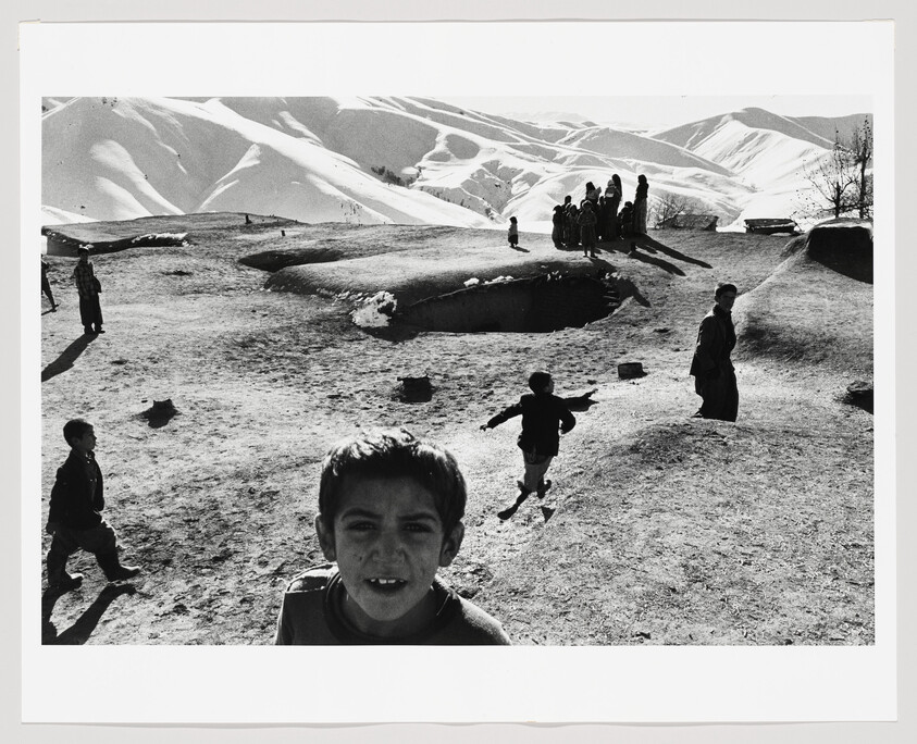A boy looks toward the camera while other children run and gather on snowy hills.