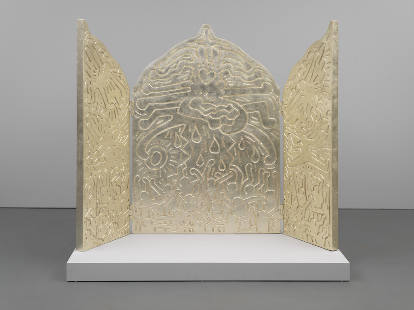 A three-paneled, freestanding sculpture with intricate relief designs on a white display platform against a grey background. The central panel is taller and features a symmetrical, ornate pattern, while the side panels have matching designs that complement the centerpiece. The material appears to be metallic with a golden sheen.