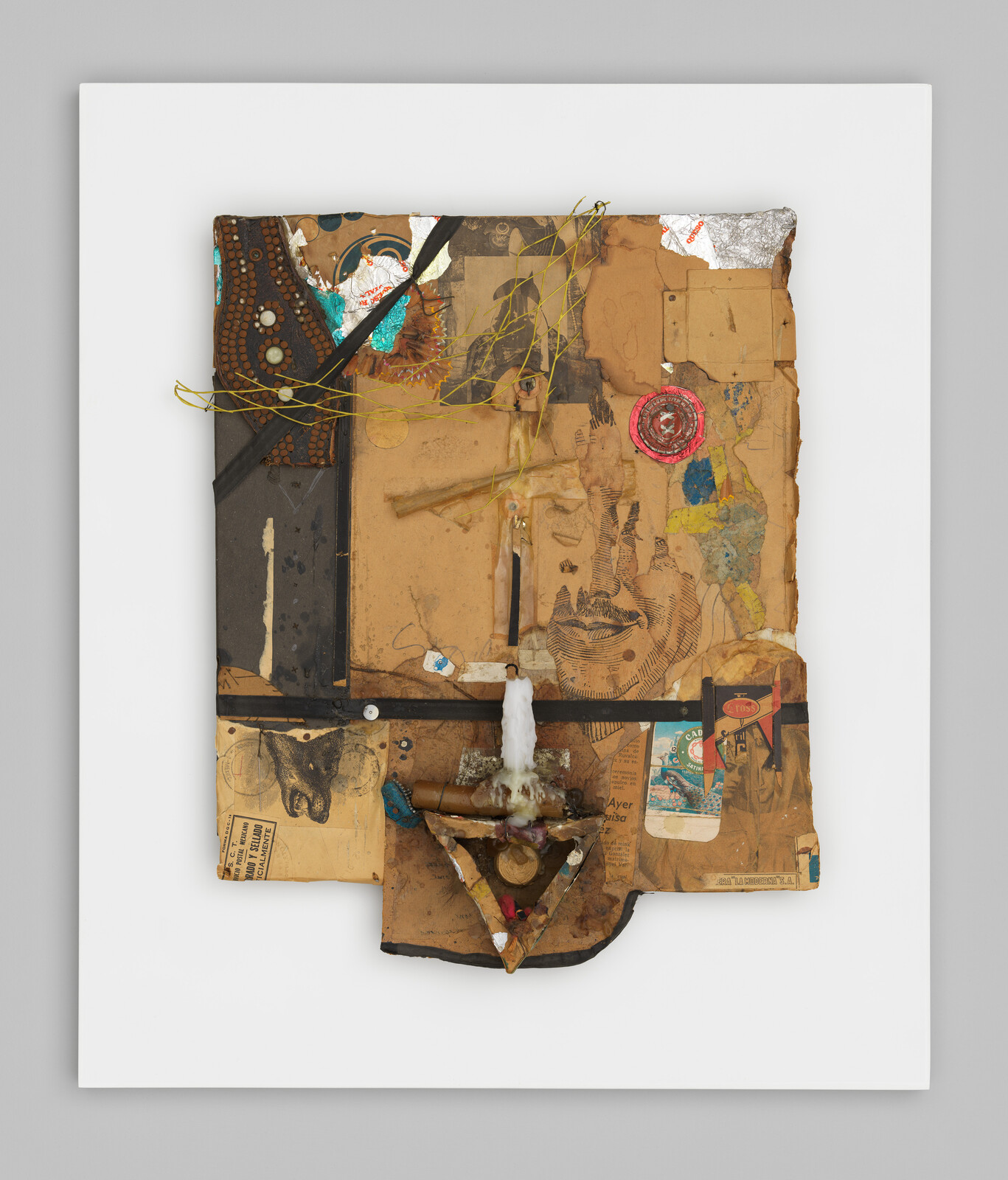 Mixed-media collage on a white board featuring cardboard, a sketched face, a candle, and layered objects.