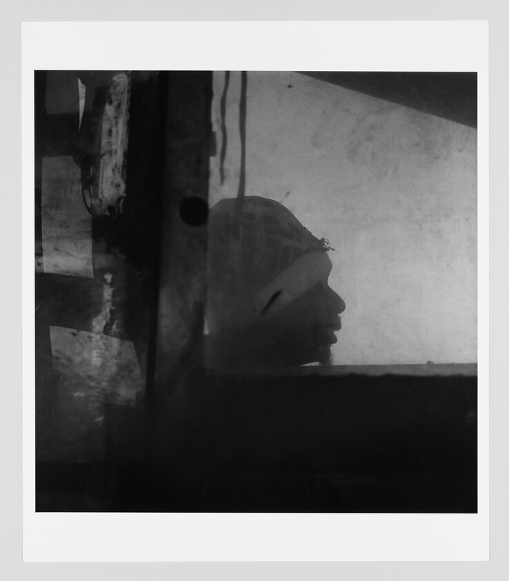 Silhouetted person in profile wearing a headscarf, seen through a grimy window.