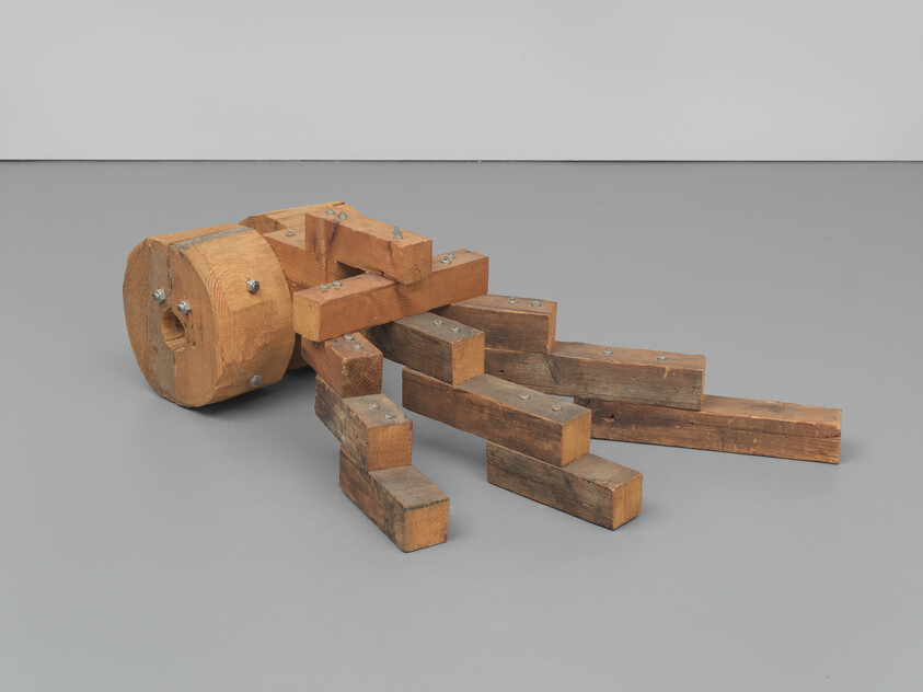 A wooden abstract sculpture with a cylindrical base and several bolted rectangular beams extending outward.