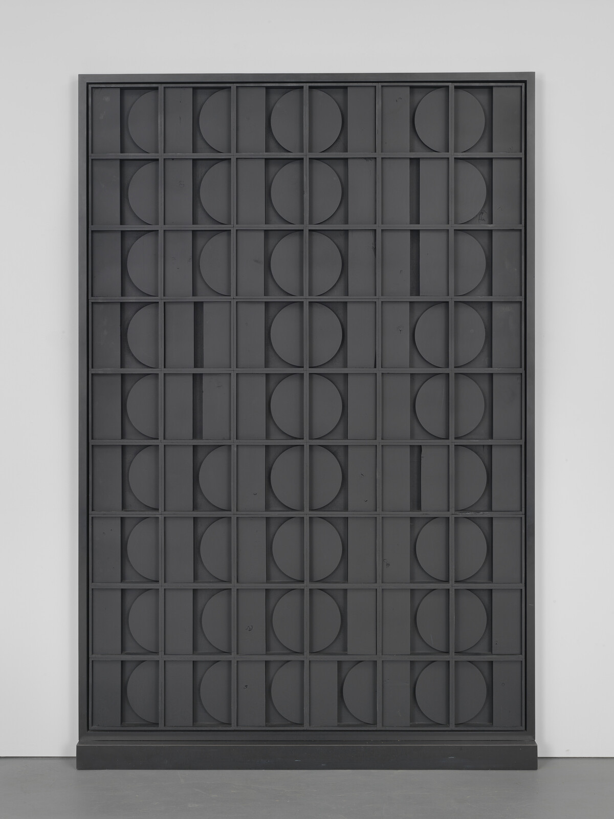 Tall black wooden panel with a grid of squares containing semicircles forming circular patterns.