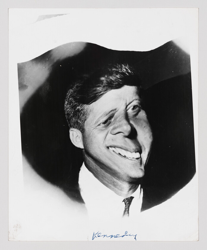 Smiling man in a suit with distorted, warped facial features against a dark background.