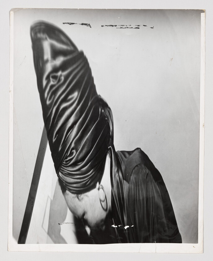 Person wearing a tall satin turban and hoop earring bowed forward.