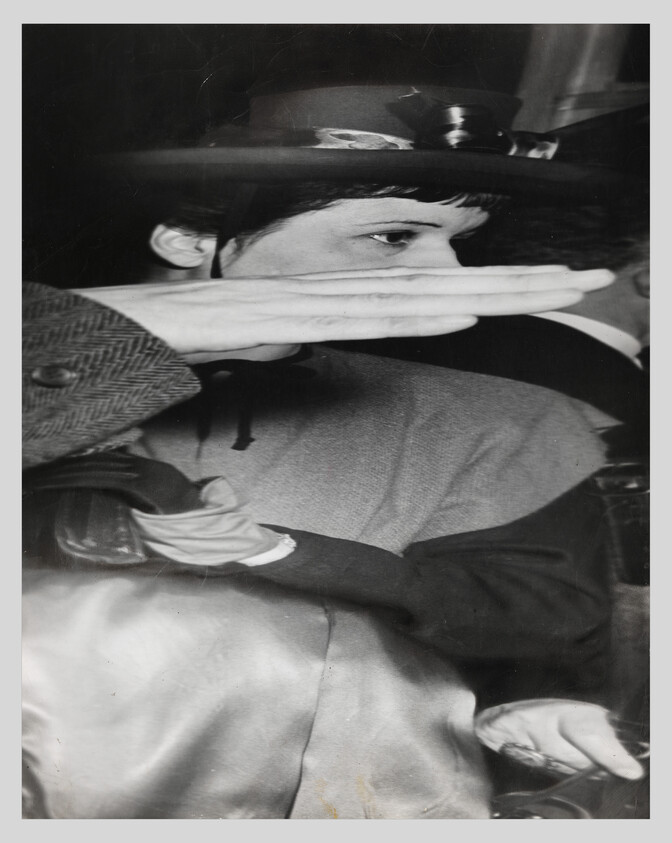 Woman wearing a hat shields her face with a hand while sitting in a crowded vehicle.