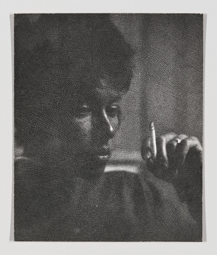 Person holding a cigarette near their face while looking to the side in grainy black-and-white.