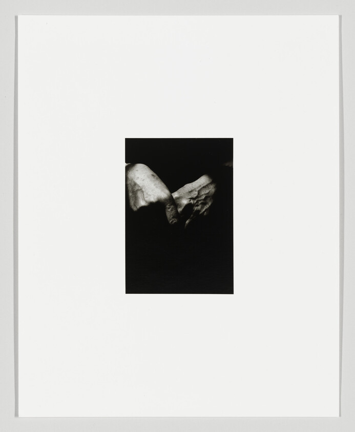 Two aged hands gently clasp each other against a dark background in the center of a white page.