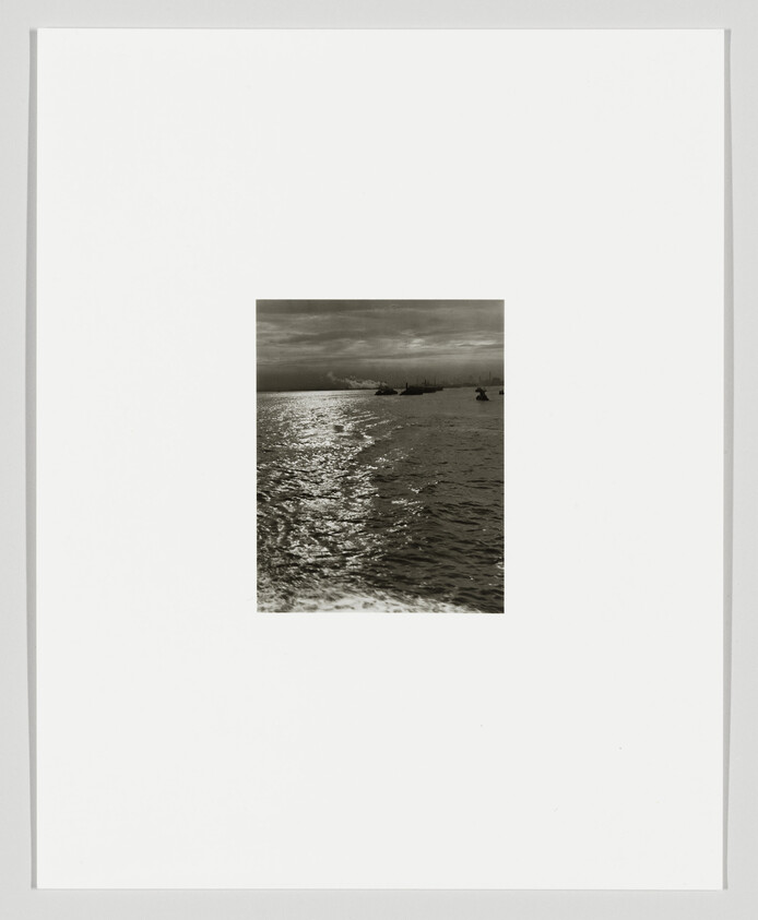 Sunlit ocean waves lead toward small boats on the distant horizon under a cloudy sky.