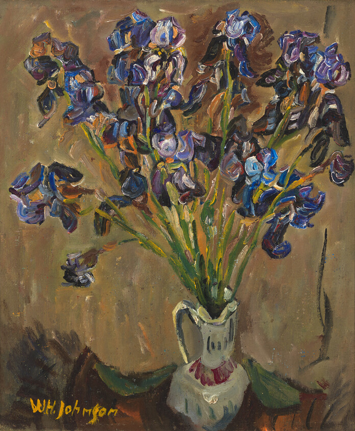 A bouquet of purple irises in a white pitcher against a brown background.