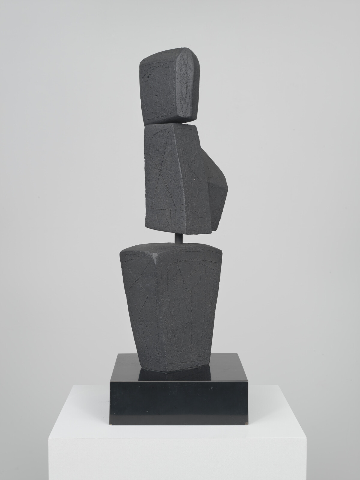 Tall abstract dark sculpture of stacked geometric shapes resembling a simplified human figure on a pedestal.