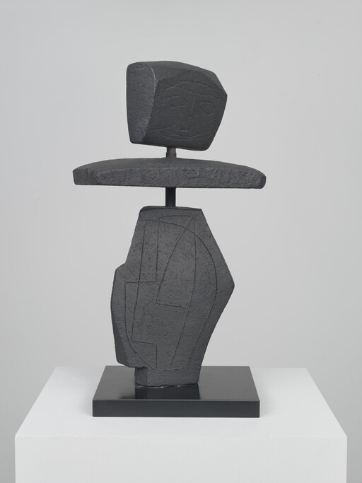 Dark abstract stone sculpture with a carved face on top layered over a geometric base.