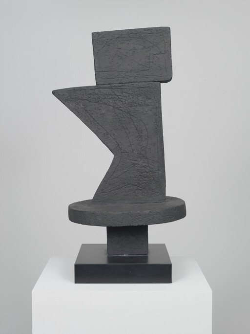 Abstract dark stone sculpture with geometric shapes standing on a square black base and white plinth.