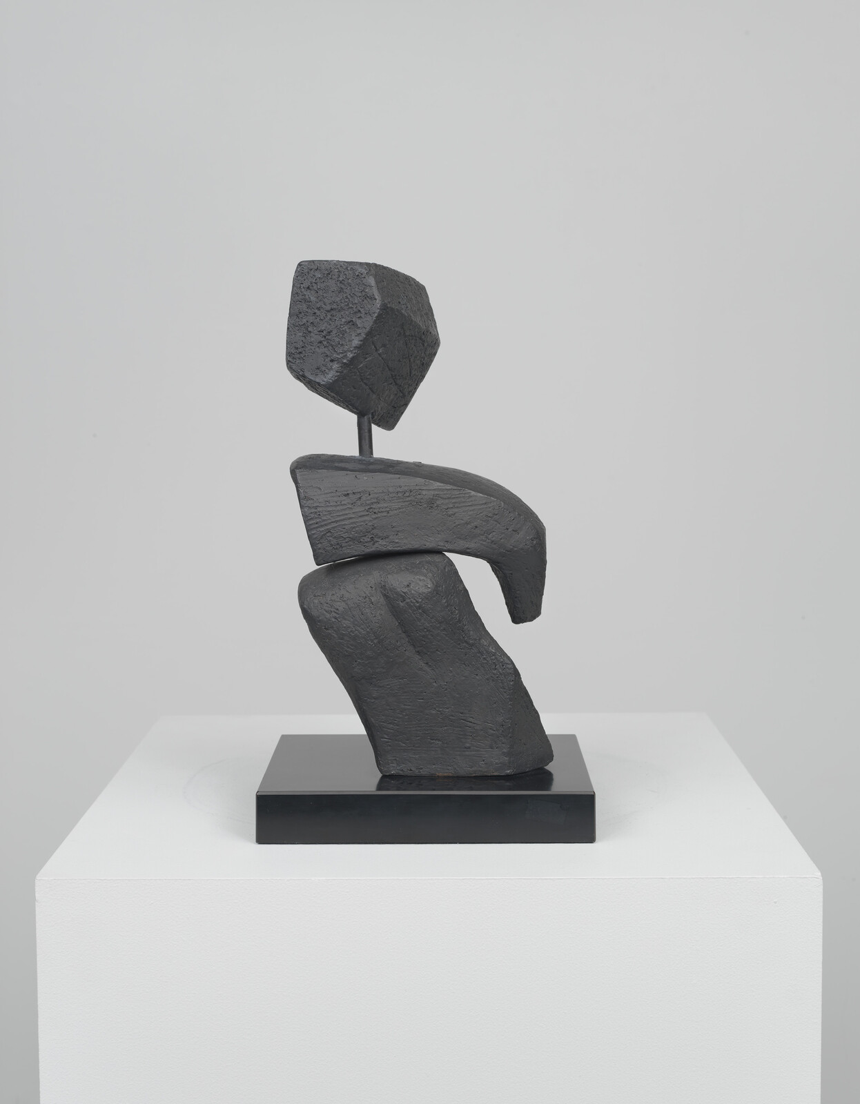 Abstract black stone sculpture of stacked geometric forms balancing on a black base atop a white pedestal.