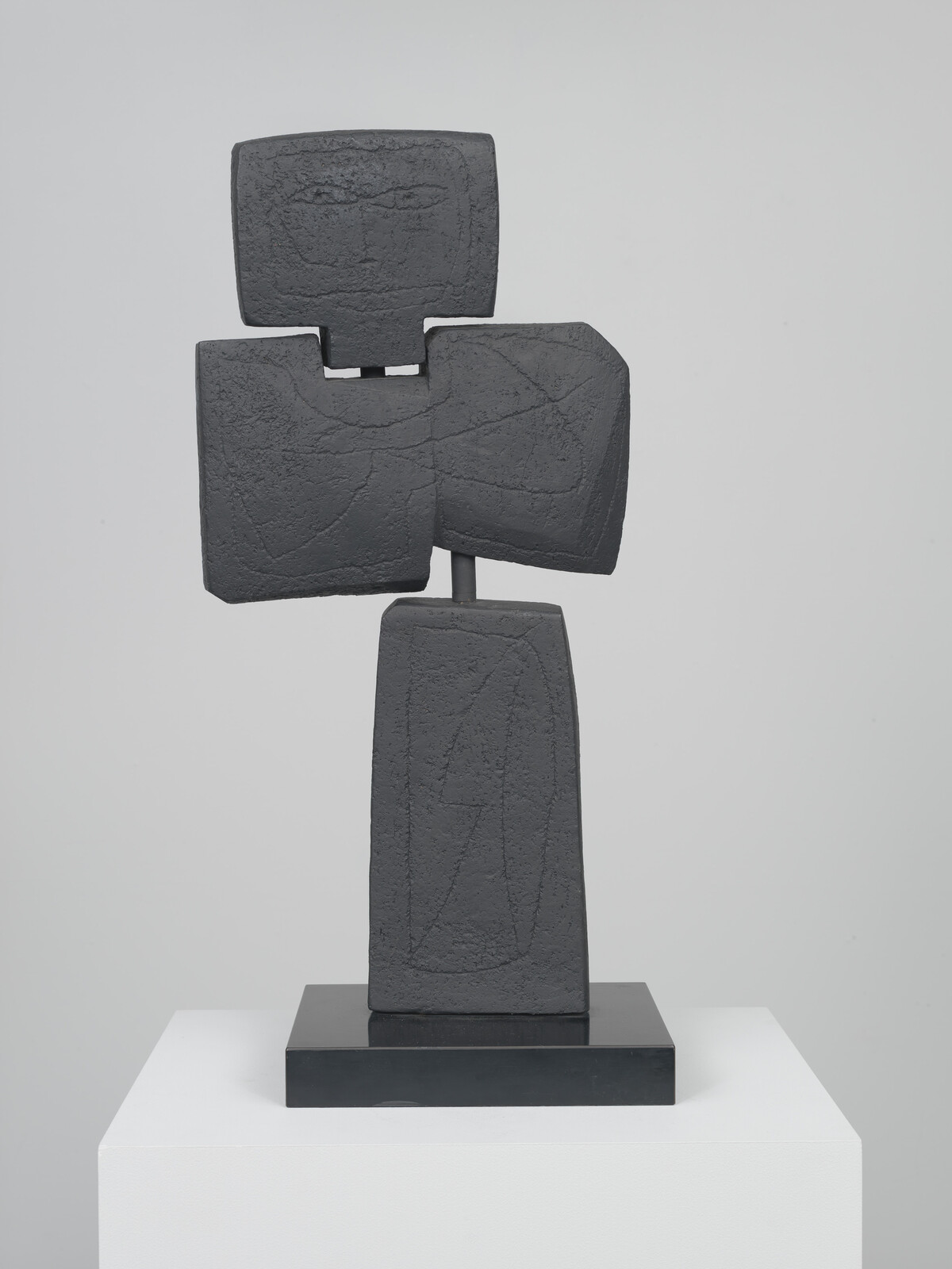 Abstract dark stone blocks stacked to suggest a stylized human figure on a black pedestal.