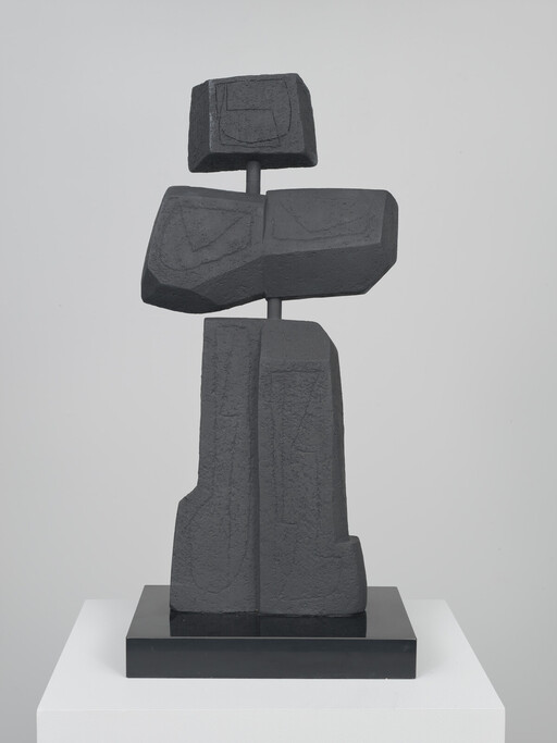 Tall abstract dark stone sculpture composed of stacked geometric blocks on a black base.