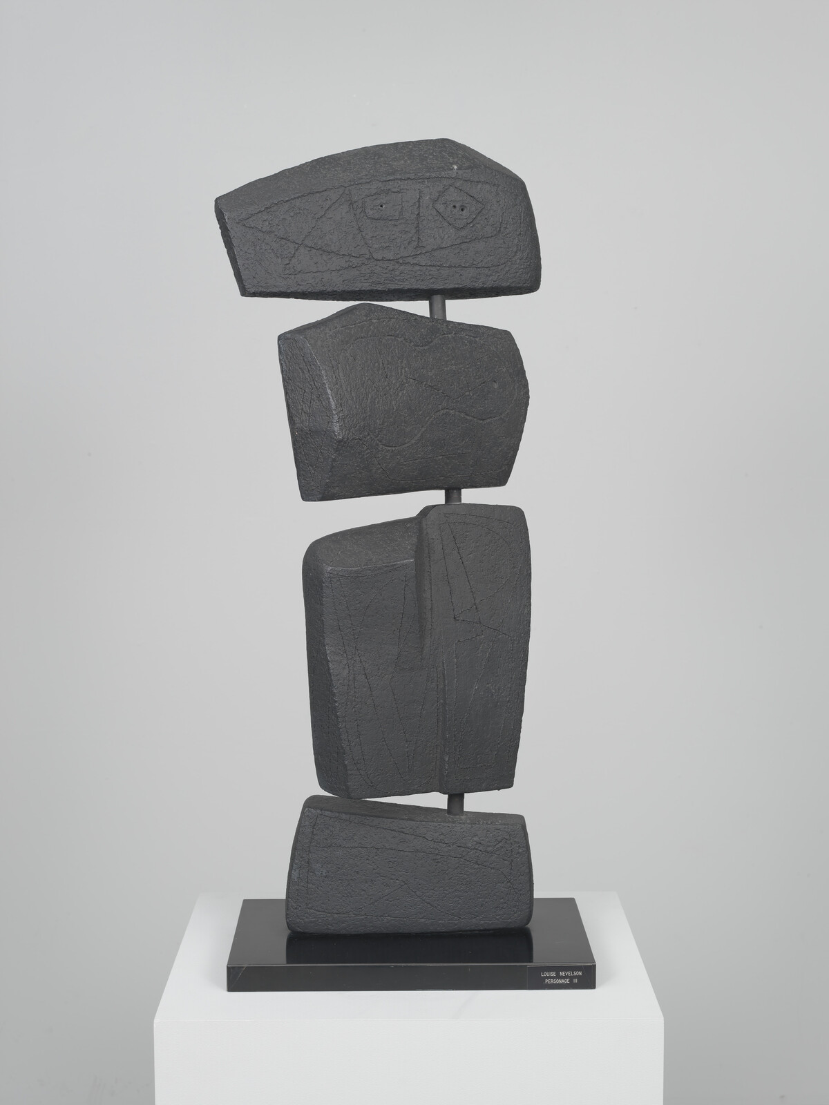 Abstract stacked black stone sculpture composed of four blocky forms balanced on a metal rod.