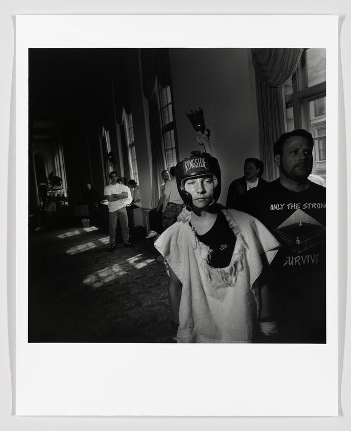 A young boxer wearing Ringside headgear and a towel stands in a hallway before a match.