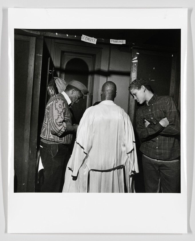 Three men stand in a doorway as two adjust a robe on the man in the center.